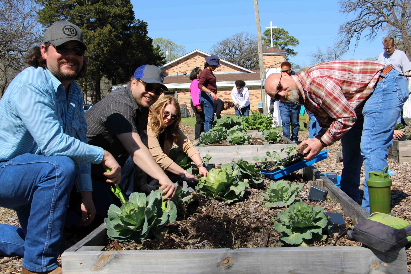 Group of people outside bending over to look at plants in a raised flower bed 