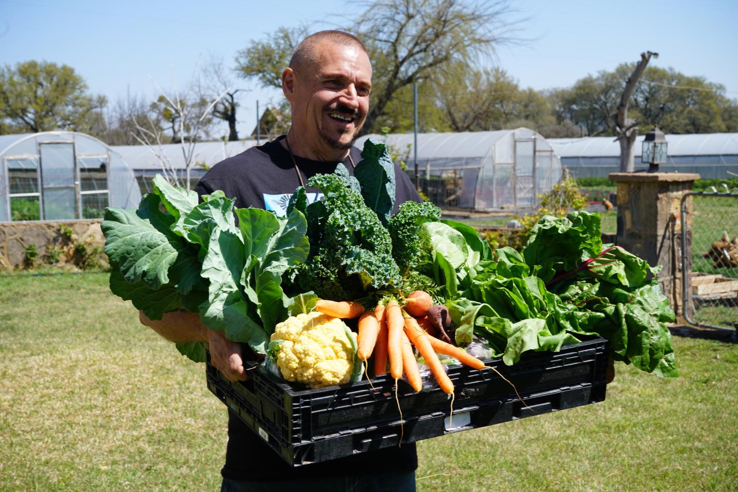 Man standing outside holding a container of fresh vegetables