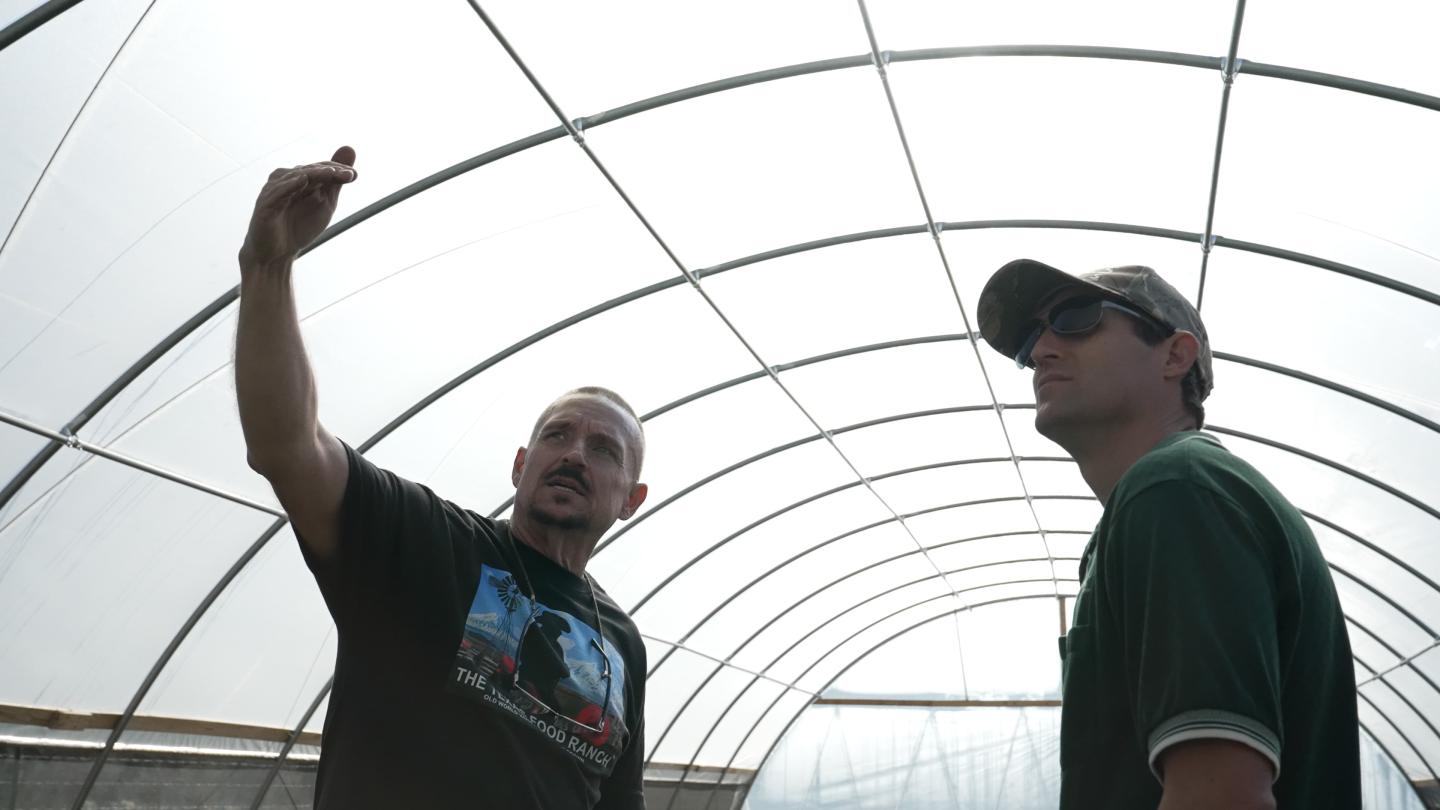 Two men stand outside under a high tunnel