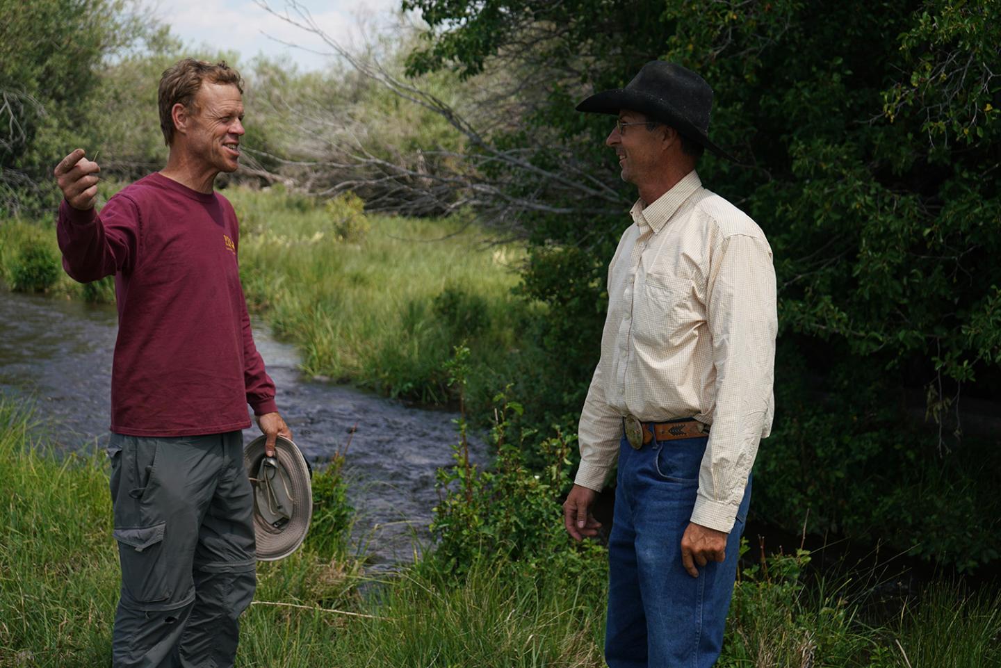 Two men stand near a creek.