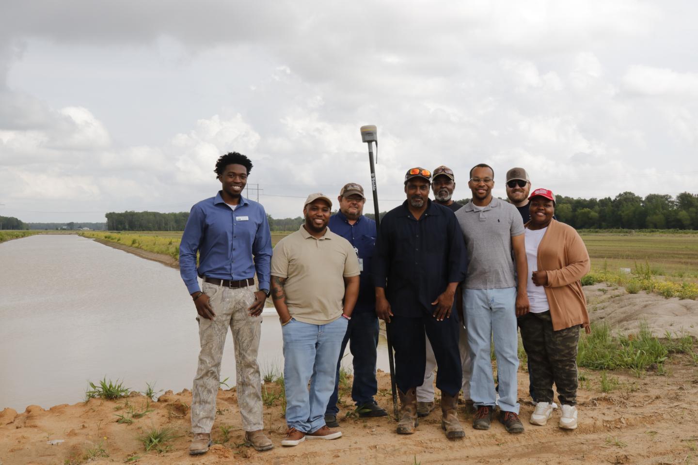 A group of NRCS field personnel pose in front of an irrigation reservoir and a field.