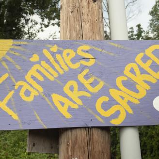 Purple and yellow handmade sign that reads "Families are Sacred"