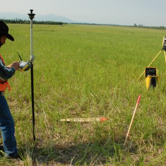 A man uses survey equipment in a field in Alaska. 
