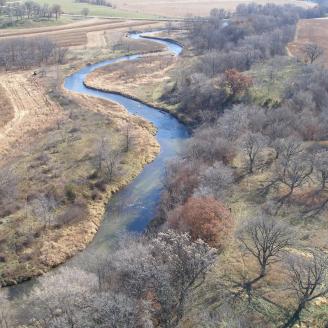 Aerial view of a river running through agricultural land, with fields and trees.