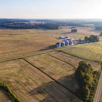 Aerial view of cropland fields, with grain bins near the center of the photo and stands of trees in the foreground and background.