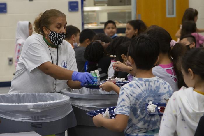 A cafeteria monitor helps students sort food waste.