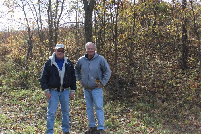 landowner and district conservationist posing in front of wooded area
