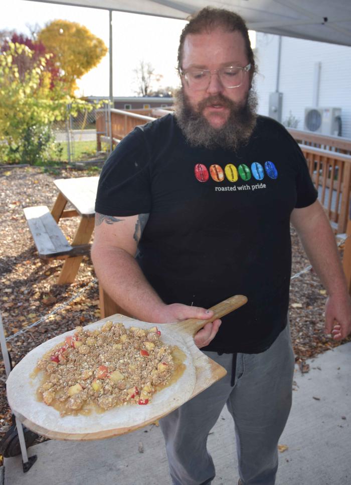 New City Neighbors Cafe Coordinator Luke De Haan prepares to place an apple dessert pizza in the outdoor woodburning oven.