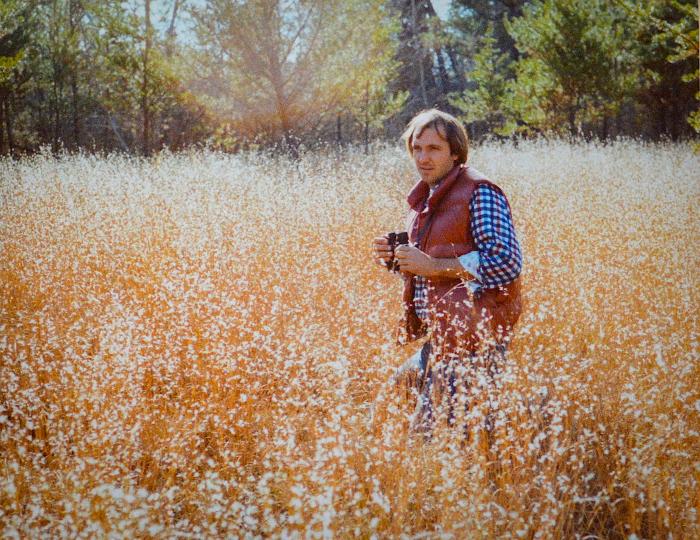 Man in a red vest and blue gingham shirt standing in a prairie