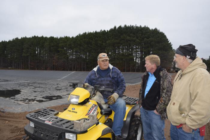 Two men standing next to a man sitting on an ATV.