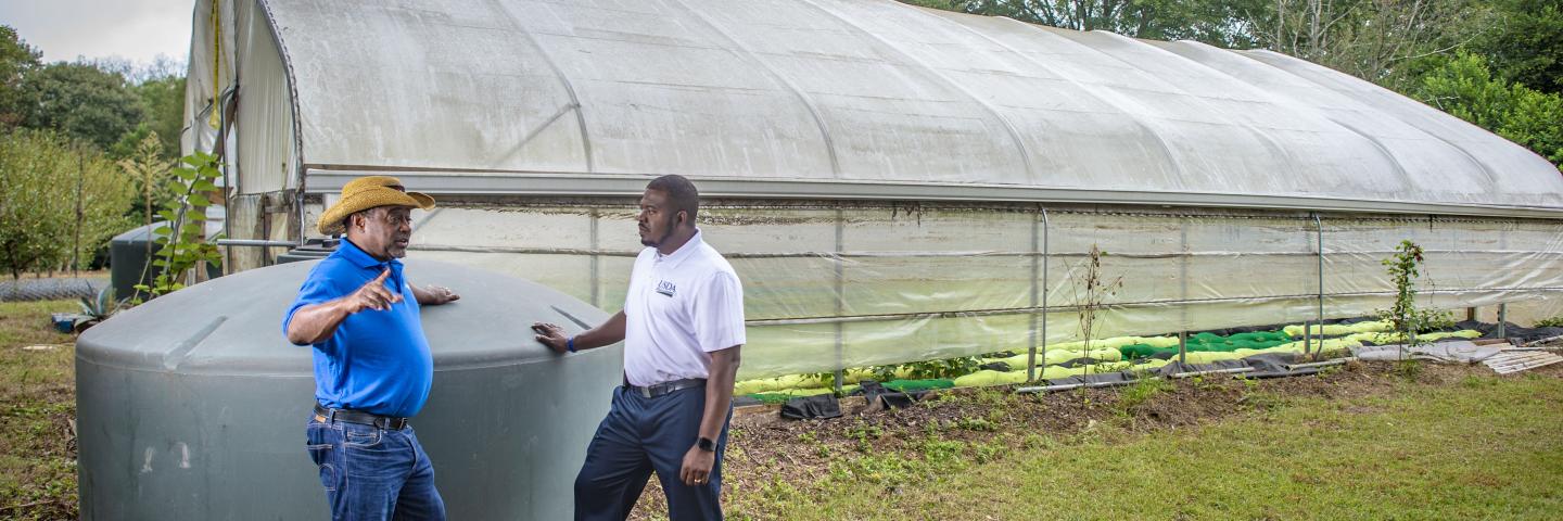 two men standing next to a high tunnel talking