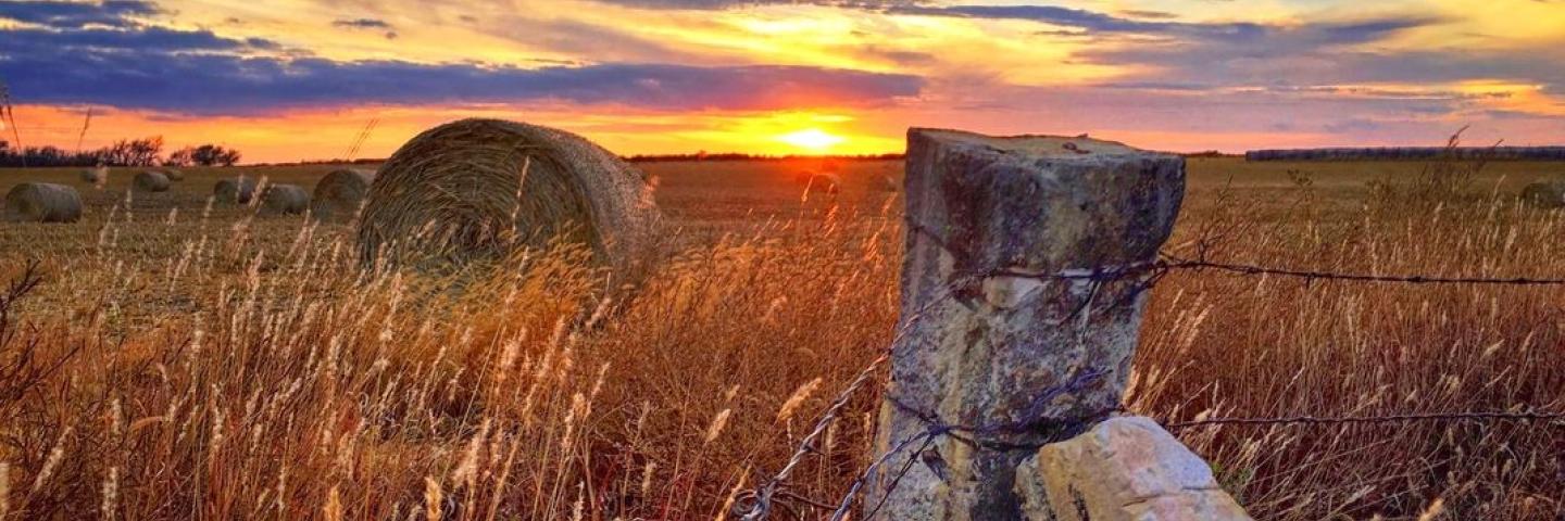Kansas sunset with limestone fence posts and hay bales