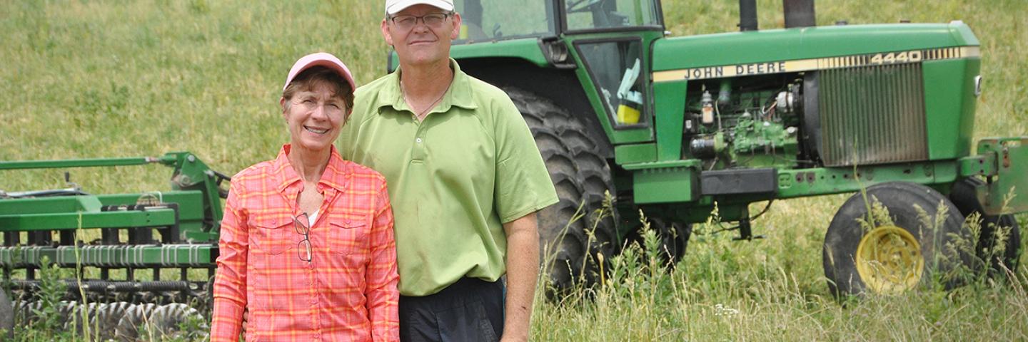 Mike McDonald and his wife, Janet, stand in a field by a tractor.