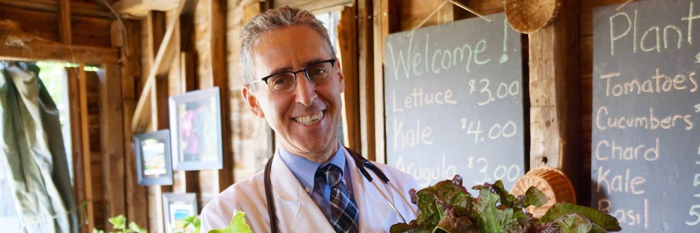 Dr. Ron Weiss smiles and holds up produce.
