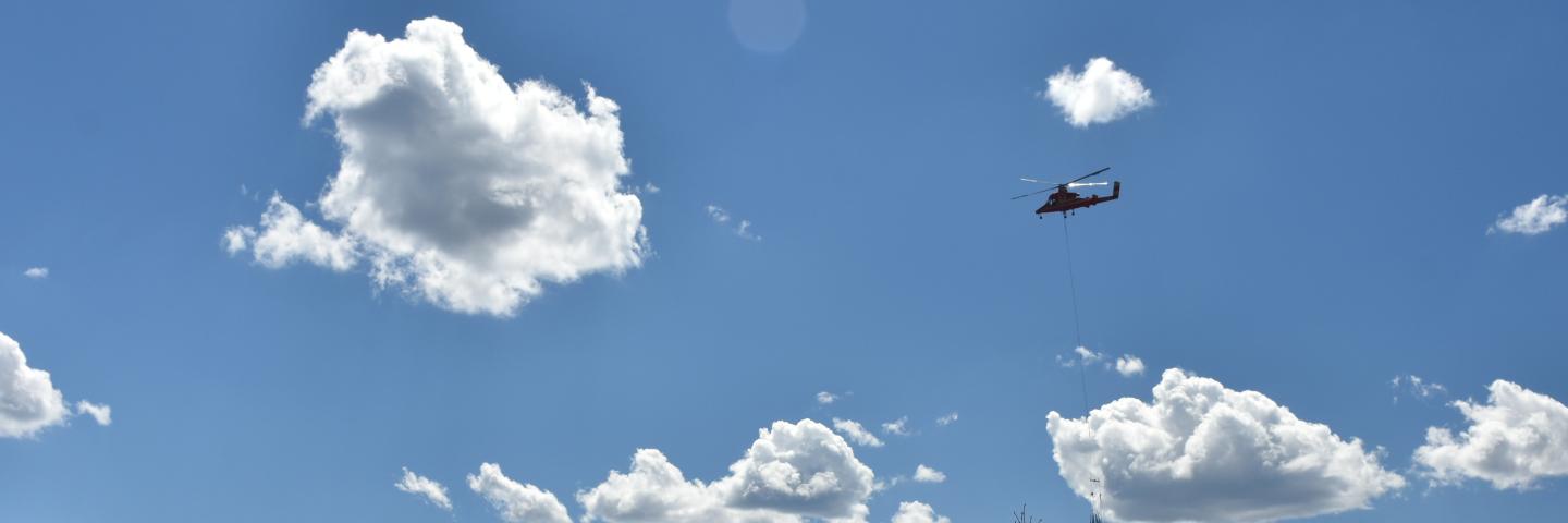 Helicopter silhouette carrying mulch over forest land burned by wildfire 