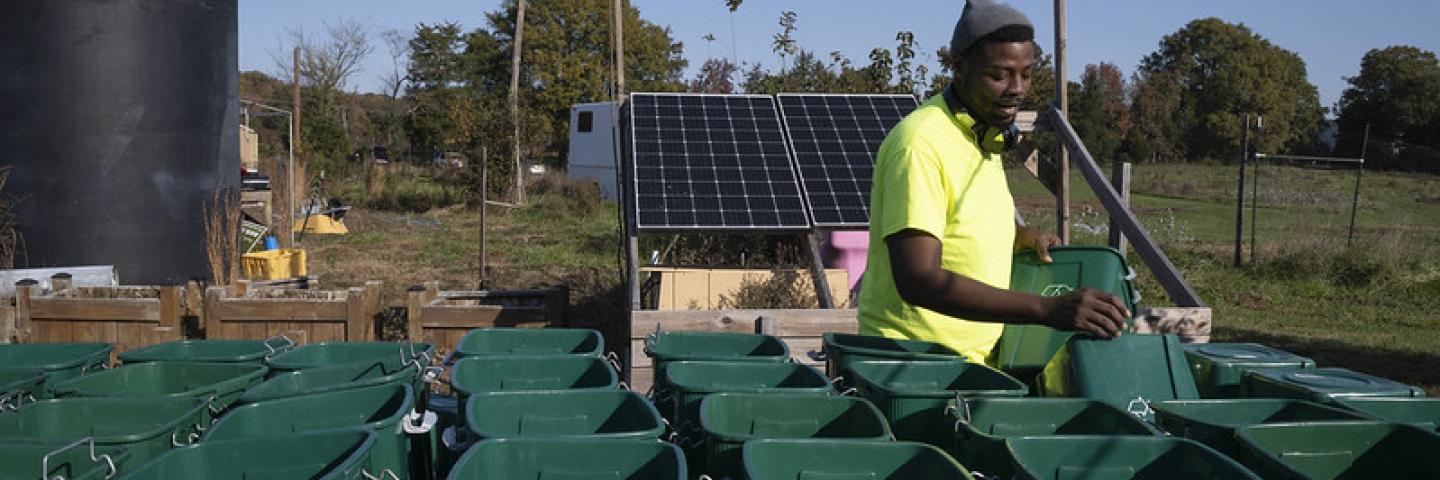Young African-American man setting up rows of two-wheeled composting bins