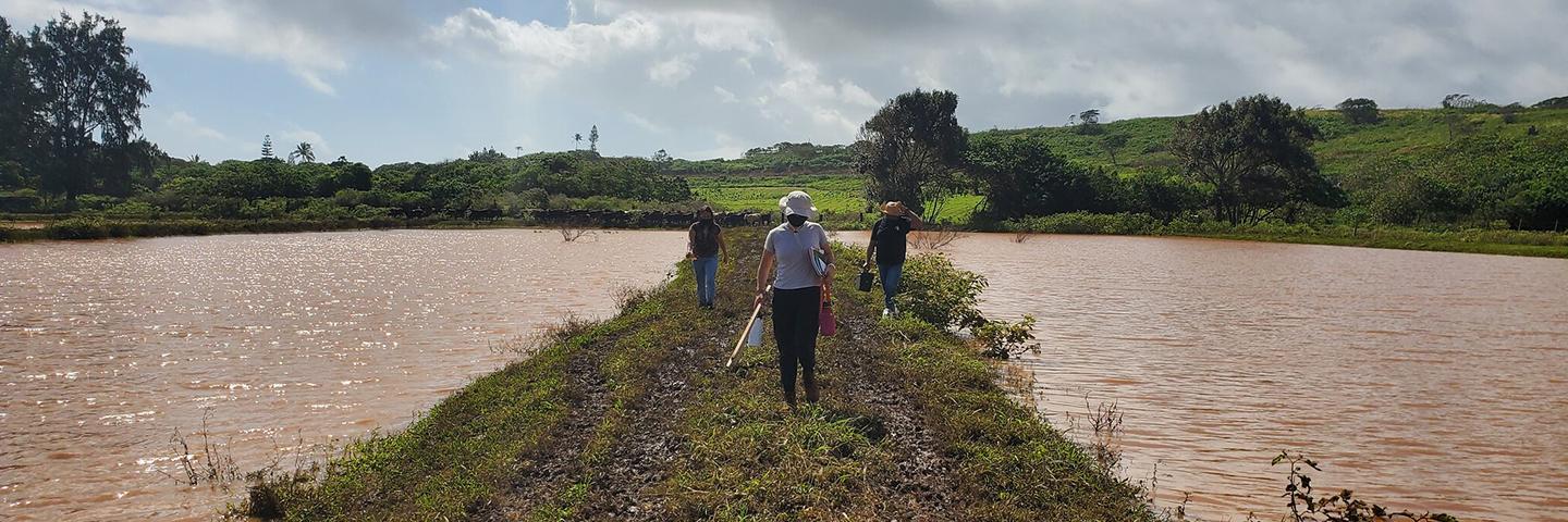 A photo of 3 people walking on a trail with water on both sides.