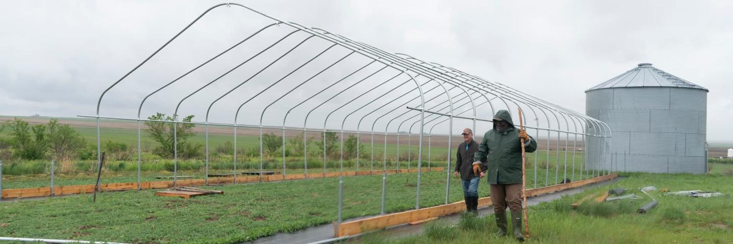 Two men standing in a field next to the frame of a high tunnel