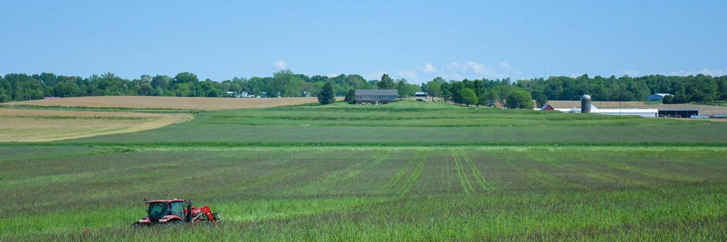 Large fields with a tractor in the foreground, and barns and silos in the background