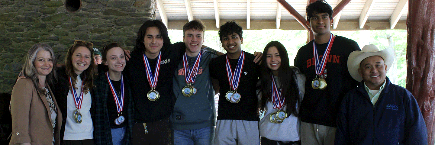 2023 Rhode Island Envirothon winners from the Wheeler School (team 1) display their medals with NRCS State Conservationist, Pooh Vonkhamdy (right), and their teacher (left).