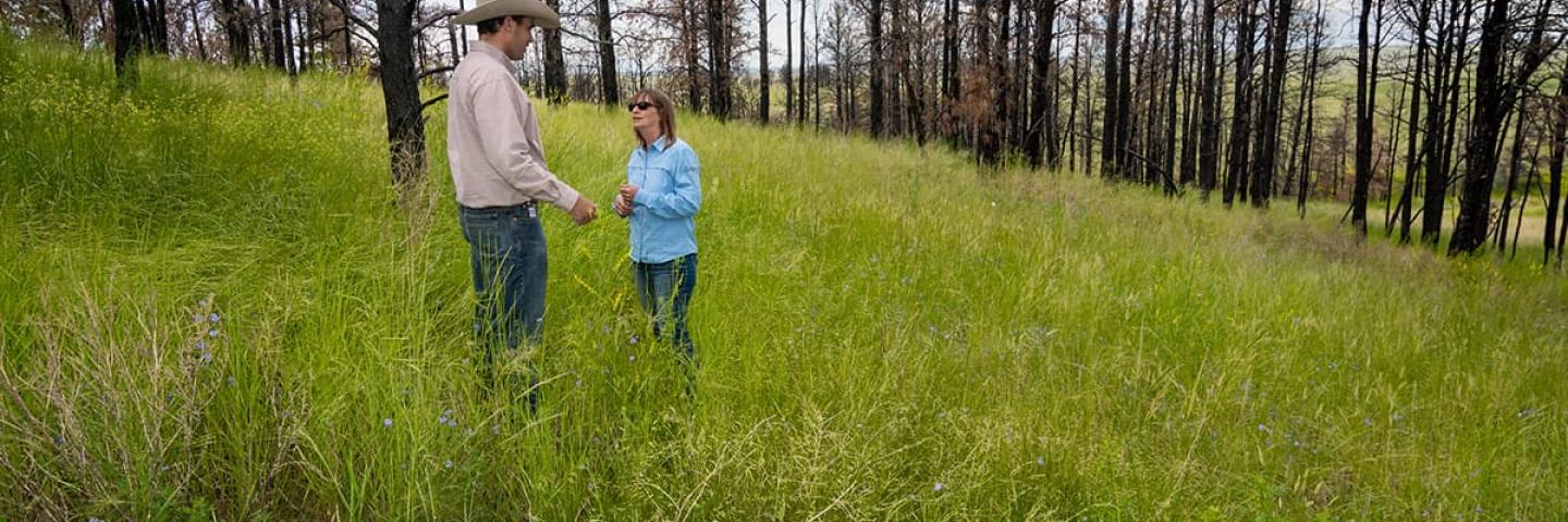 NRCS employee and landowner walk an area with burned trees.