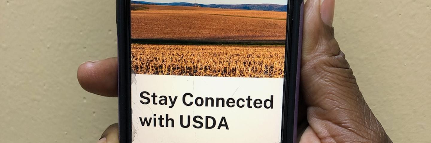 hand holding smart phone with Farmers.gov webpage open saying 'Stay Connected with USDA'