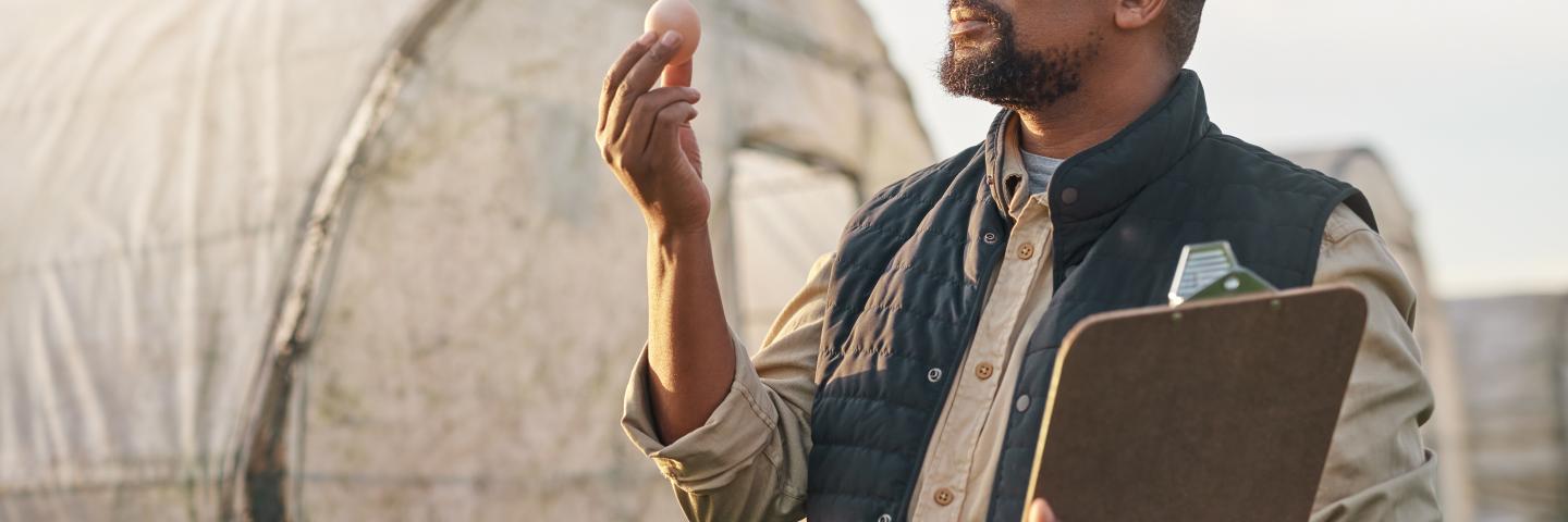 Farmer examining an egg while holding a clipboard