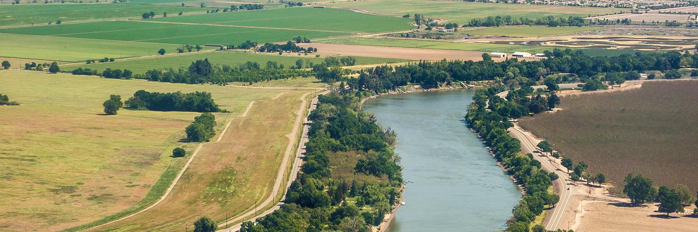 Aerial photo of a river buffered by trees with various land uses, including agricultural land, on both sides. Roads are present on both sides of the river.