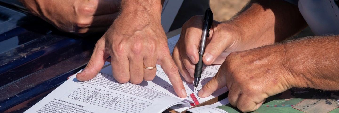 NRCS employee hand pointing with his pinkie to signing block customer signing block where customer is about to sign Water and Sediment Control Basin, conservation practice 638