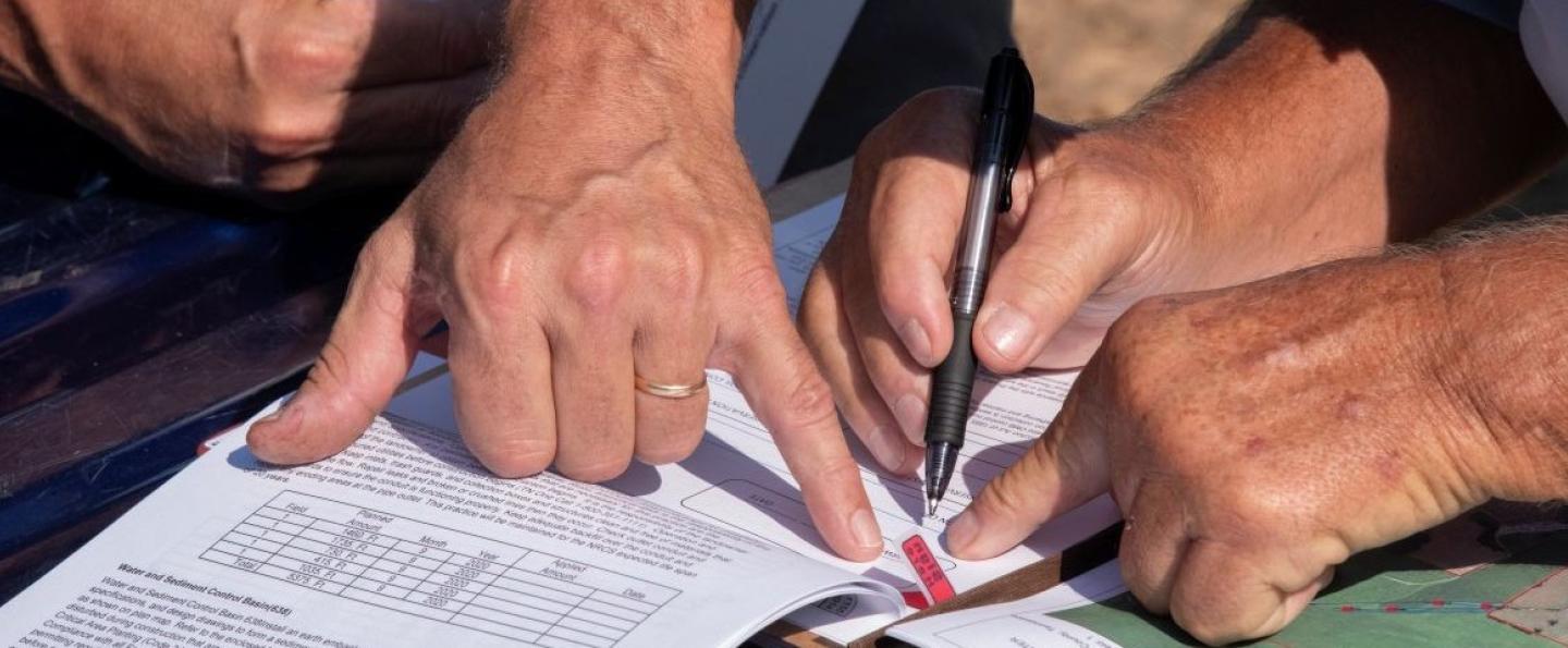 NRCS employee hand pointing with his pinkie to signing block customer signing block where customer is about to sign Water and Sediment Control Basin, conservation practice 638