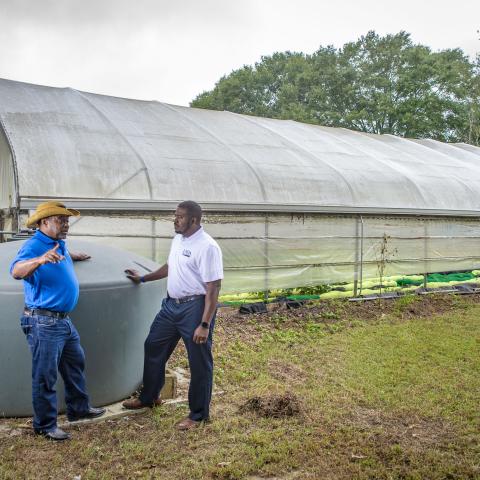 two men standing next to a high tunnel talking