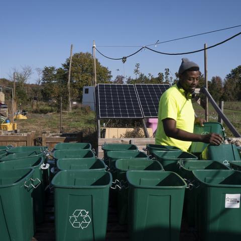 Young African-American man setting up rows of two-wheeled composting bins