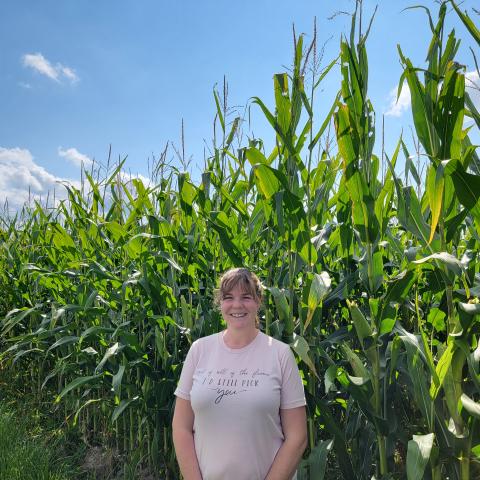 Woman in a light pink shirt standing in front of a corn field