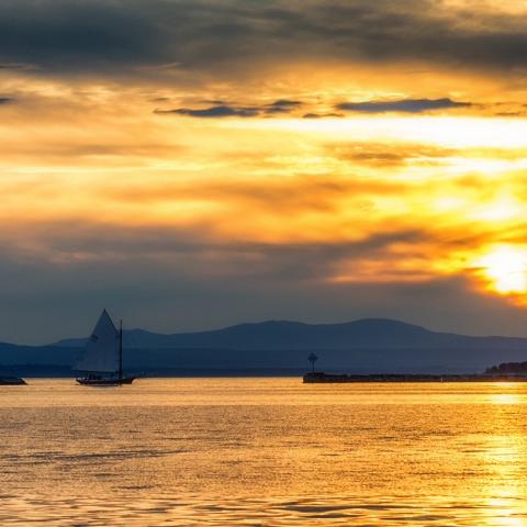 Small sailboat in water and lighthouse on island in Lake Champlain at sunset