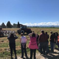 several people standing in a line observing farm equipment 