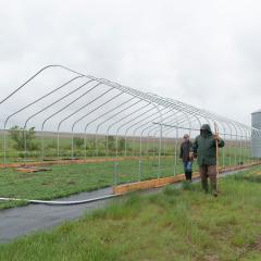 Two men standing in a field next to the frame of a high tunnel