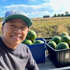 Man sitting in front of bins of watermelon on his farmland