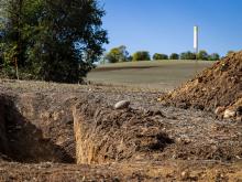 Soil pit with farm landscape and trees in the background