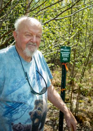 Landowner Robert ‘Bob’ Kidder poses for a photo next to a marker delineating his conservation property in Stark, N.H. May 13, 2022.  Kidder recently closed on an easement through the USDA’s Natural Resources Conservation Service that ensures the land will be safe from development in perpetuity. Kidder, who grew up on the property smiles at the thought of protecting the land for generations to come. (USDA photo by Jeremy J. Fowler, NRCS, N.H.)