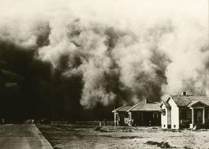 A black cloud of dust approaches a house.