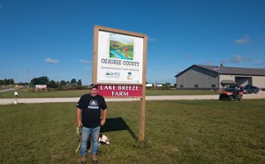 Man standing in front of sign on his farm
