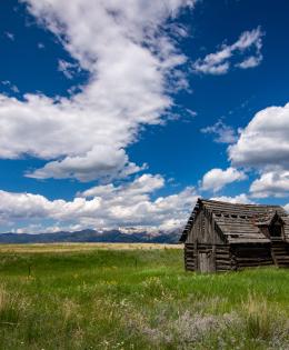 Log cabin in a wide field with mountains in the distant background