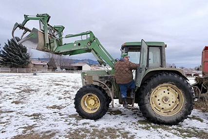 Bob Sutherlin climbs in a tractor to feed cattle.