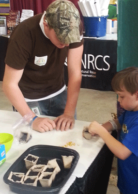 Volunteer helping child plant seed at State Fair booth